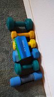 Six pairs of hand weights in various colors (green, yellow, blue) and sizes laid out on carpet