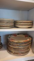 Shelved stacks of Franciscan Desert Rose bread plates and dinner plates showing floral pattern and gold rims