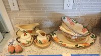 Full assortment of Franciscan Desert Rose serving pieces including gravy boat, sugar bowl, creamer, salt and pepper shakers, salad bowls, glass bowl and serving platter displayed on kitchen countertop.