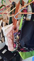 Photo showing several hanging handbags and totes on clothes hangers including an off-white tote with black design, reddish patterned beige handbag, floral print tote, and solid black handbag