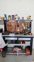Front view showing Husky workbench with riser shelf, pegboard back panel, and various tools hanging and placed on and around the bench.