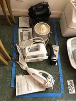 Wide view of lot showing Hamilton Beach soft scrape mixer, Oster juice extractor, Cuisinart hand mixer, Chef's Choice sharpener and associated manuals.