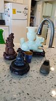 Lot arranged on countertop showing jade dragon on wooden stand, wooden figurines, metal Buddha, and metal shoe-shaped ashtray