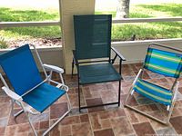 Three collapsible metal outdoor beach chairs on tiled floor, arranged side by side under covered patio.