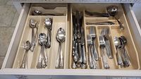 Top-down view of drawer showing separated cutlery pieces including forks, knives, teaspoons, tablespoons, and salad forks arranged in compartments