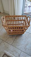 Side view of rectangular wicker basket with open weave, two handles, and wheels.