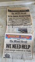 Old Miami Herald newspapers with hurricane headlines and black and white photos, showing devastation and troop deployment in response to hurricanes.