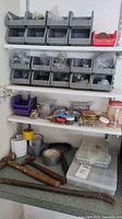 Wide view of shelf with multiple plastic bins containing screws, nails, small hardware pieces, rolls of tape, and two large rusty hammers on countertop.