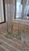 Two tall, green-tinted clear glass vases with linear patterns, displayed on wicker surface.