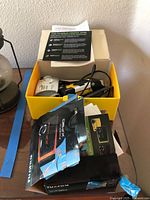 Top-down photo showing a yellow box containing a Kodak Power Flash camera with accessories and cables, along with a Fuji Film instruction booklet and case.