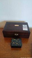 Two vintage jewelry boxes on wooden surface, larger wood box and smaller black painted floral box