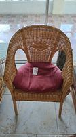 Front view of a natural wicker chair with pink padded seat cushion.