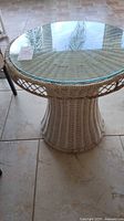 Front view of the round wicker table with the clear glass top, showing the full profile and top surface.