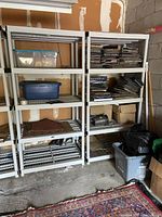 Two gray plastic shelving units positioned side by side inside a garage or storage area. Shelves hold various items such as boxes and containers.