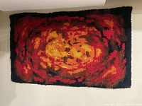 Full view of the rectangular hooked wool rug showing abstract red, orange, brown pattern and black border.