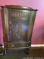 Front view of antique oak armoire with detailed carved front door and drawer below.
