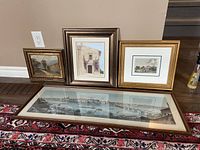 Four framed art pieces placed on floor showing one large panoramic print and three smaller framed artworks.