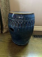Side view of the blue textured ceramic seat showing tassel motif and drainage hole near the bottom.