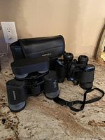 Two pairs of binoculars and one carrying case on a countertop, featuring black Bushnell and Tasco binoculars.
