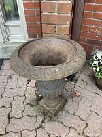 Full view of the rusty cast iron planter showing the decorative rim and the urn shape.
