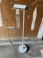 Full view of the white metal pole and base floor lamp standing against a wall