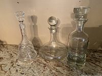 Set of three glass decanters including tall cut glass decanter, short wide decanter with round stopper, medium height clear decanter with wide stopper.