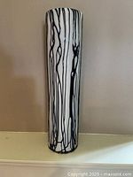 Full view of the tall white glass vase with black drip pattern against a beige wall