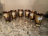 Six gold and pink decorative glasses with floral patterns arranged on a countertop.