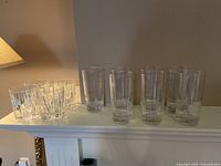 Short tumblers and tall highball glasses arranged on a shelf, showcasing intricate cut detailing on short tumblers and smooth design on tall glasses.