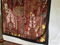 Close-up of embroidered tapestry corner showing detailed patterned patchwork and black border trim.