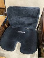 Set of a black memory foam lumbar support pillow and a seat cushion placed on a beige chair. Both items are branded Fortem with white embroidery on the front.