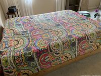 Photo of the full queen-sized quilt spread out on a bed, showing the multicolor patchwork design with various bright colors and patterns.
