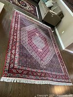Angled view of full rug on hardwood floor with sofa in background