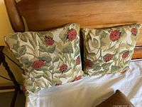 Two square cushions with a ladybug and leaf tapestry pattern on one side, displayed on a bed