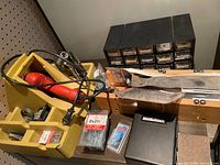 Wide view of assorted workshop tools and supplies including the yellow organizer box with drill, various screws, and black multi-drawer organizer.