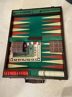 Open backgammon case showing playing surface with checkers, dice, doubling cube, two fabric dice cups, and instruction manual.