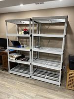 Two light gray plastic storage shelving units side by side in room, containing some items on shelves.