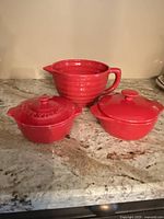 Photo of three red ceramic dishes on counter: one large handled bowl and two smaller round lidded dishes.