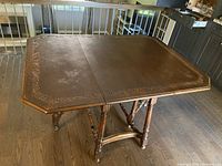 Full view of the dark brown wooden drop leaf table showing the tabletop with carved border details and turned legs.