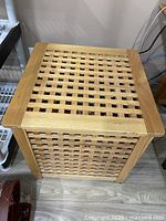 Front view of square wooden storage cube table with lattice sides and top, natural wood finish.