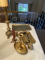 Photo of vintage brass candle holders, trays, and various brass decorative accessories arranged on a table in natural light, showing surface details, patina, and overall condition.
