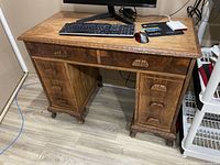 Full view of the vintage wooden desk with items on top showing its dimensions and finish, including keyboard, mouse, monitor and cards.