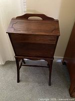 Vintage wooden sewing box with hinged lid closed, showing carry handle on top and attached stand.