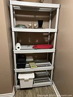 Full view of white 5-tier plastic shelving unit with various small items placed on shelves showing shelf structure and spacing.