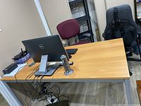 Desk fully assembled with wood top and grey metal legs, showing moderate surface wear and office chairs around.