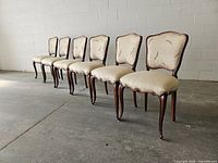 Side angle view of all six chairs showing carved walnut frames and cream upholstery.