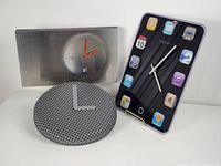 Three vintage wall clocks including a textured metal IKEA Sippra clock, a brushed stainless steel Gilad Shoham clock with red hands, and a NeXtime glass clock with smartphone app icons on black background.