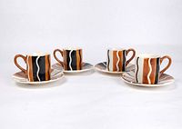 Four hand-painted espresso cups and saucers with distinct vertical stripe patterns in brown, black, orange, and white on a white background.