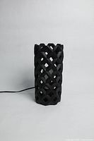 Front view of geometric tube black table lamp showing lattice pattern and electric cord.