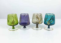 Four hand-blown colored shot stem glasses in green, purple, gray, and teal with gold decorative accents.